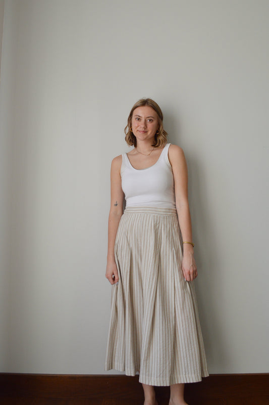 Woman holding a beige pleated skirt against a plain background