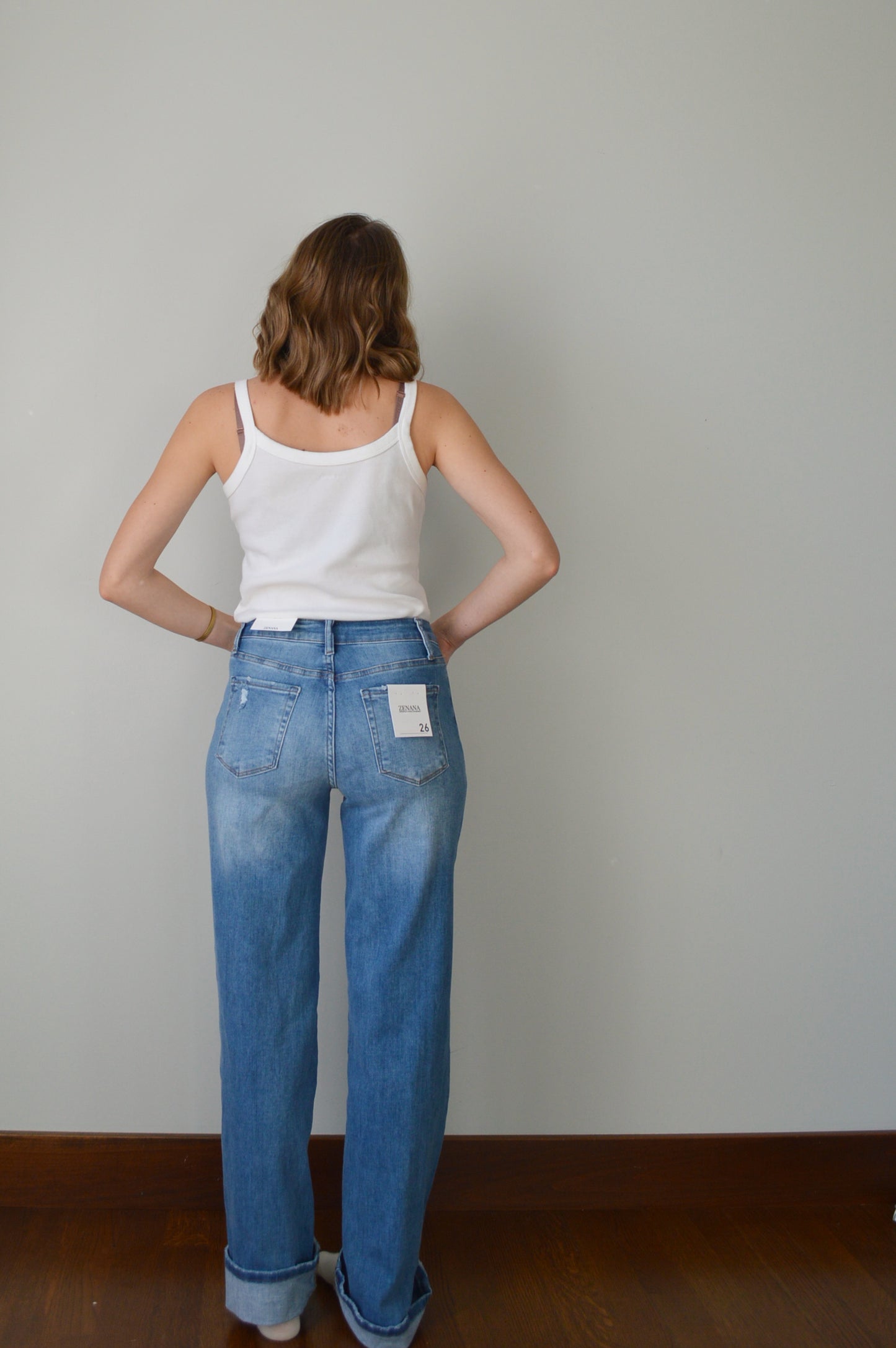 Person standing backwards wearing blue cuffed jeans and a white top against a plain background