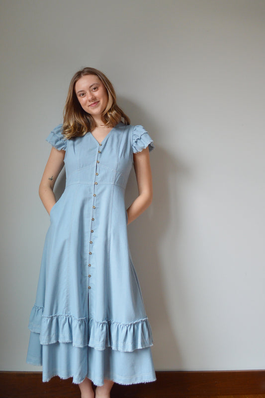 Woman wearing a light blue mid length dress standing against a grey background
