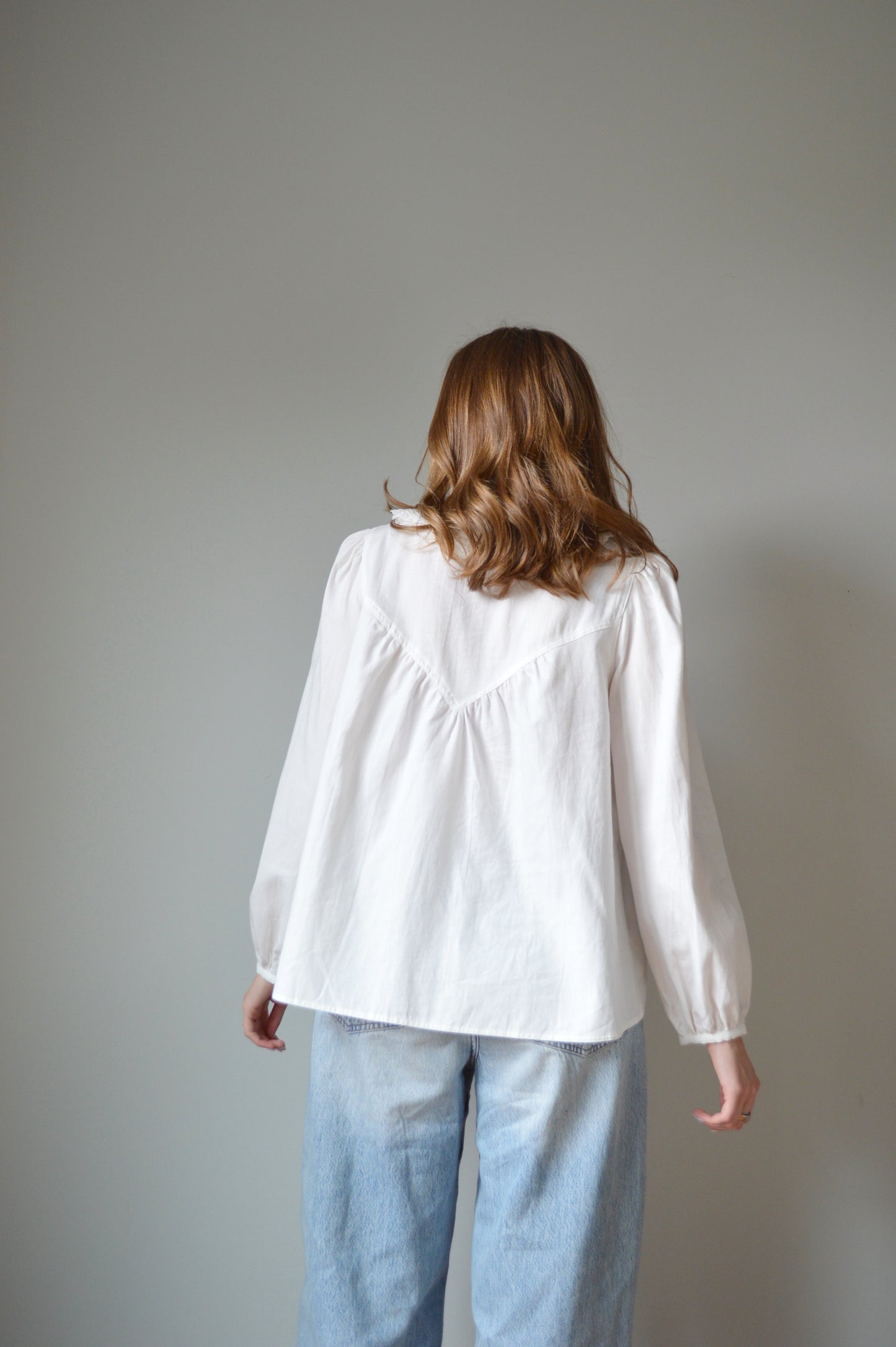 Person wearing a white shirt and blue jeans against a plain background