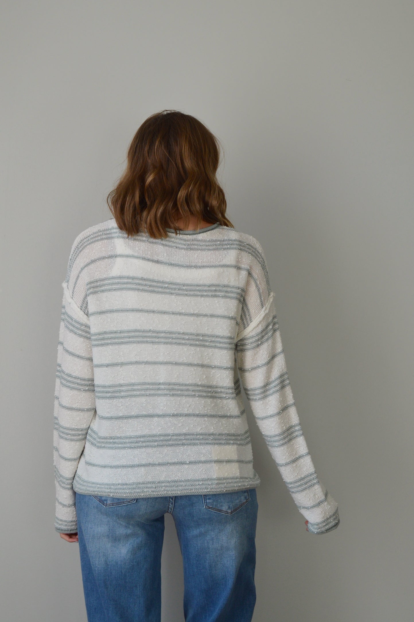 Person wearing a blue striped sweater and jeans on a plain background