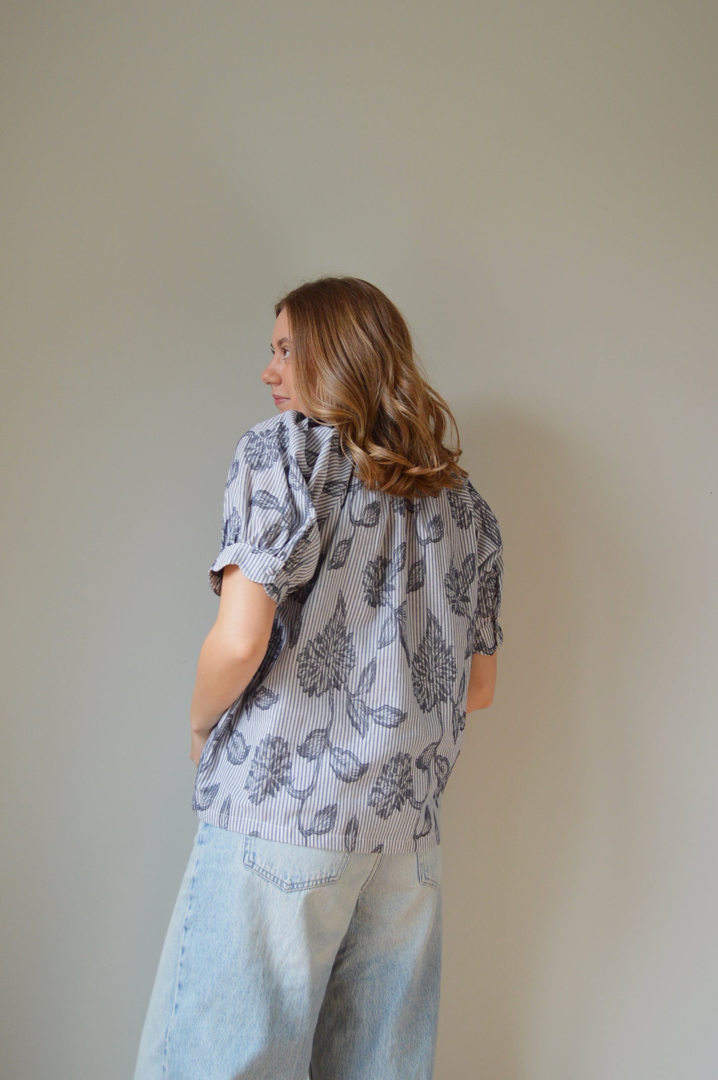 Woman wearing a blue striped blouse with navy floral design and jeans against a plain background