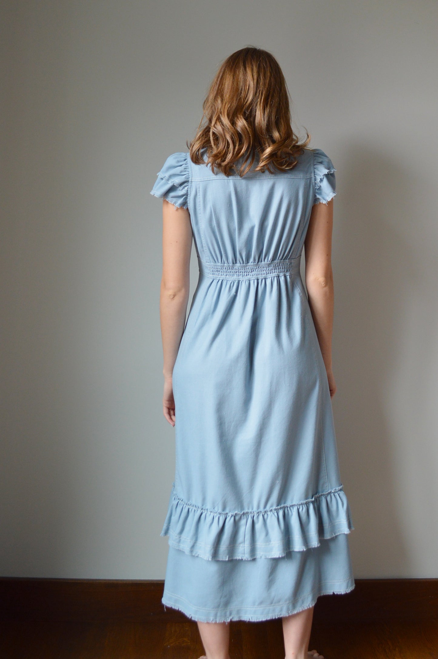 Woman wearing a light blue mid length dress standing against a grey background
