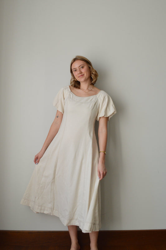 Woman wearing a cream dress standing against a plain background