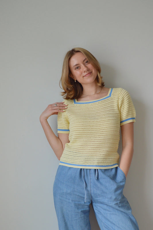Woman wearing a yellow top and blue pants against a plain background