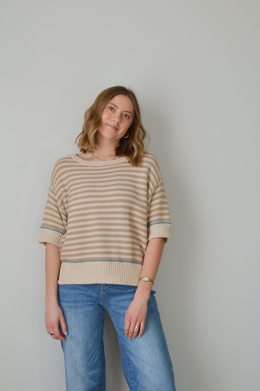 Woman wearing a tan striped sweater and blue jeans against a plain background