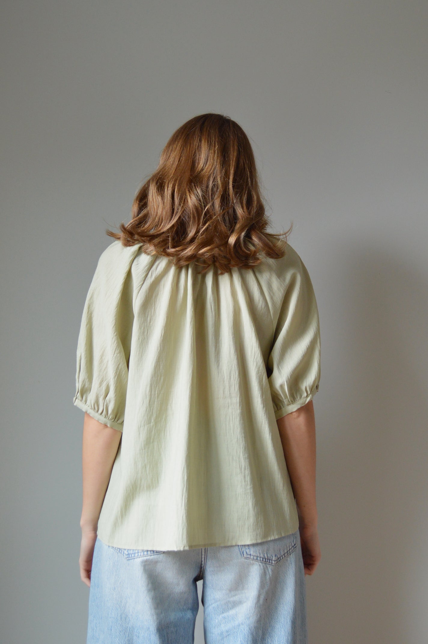 Person wearing a light green shirt and blue jeans against a plain background