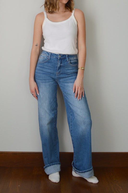 Person wearing blue cuffed jeans and a white top against a plain background