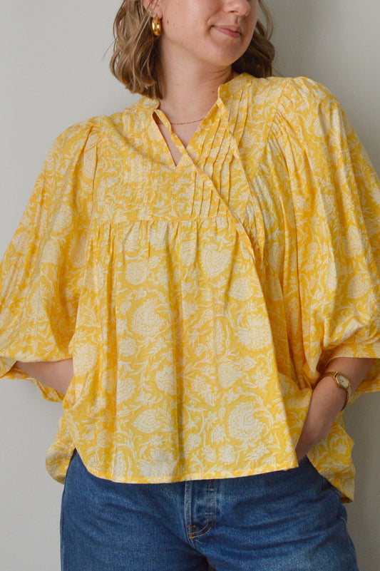 Person wearing a yellow patterned top with a plain background