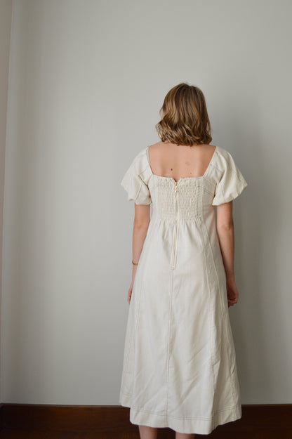 Woman wearing a cream dress standing against a plain background