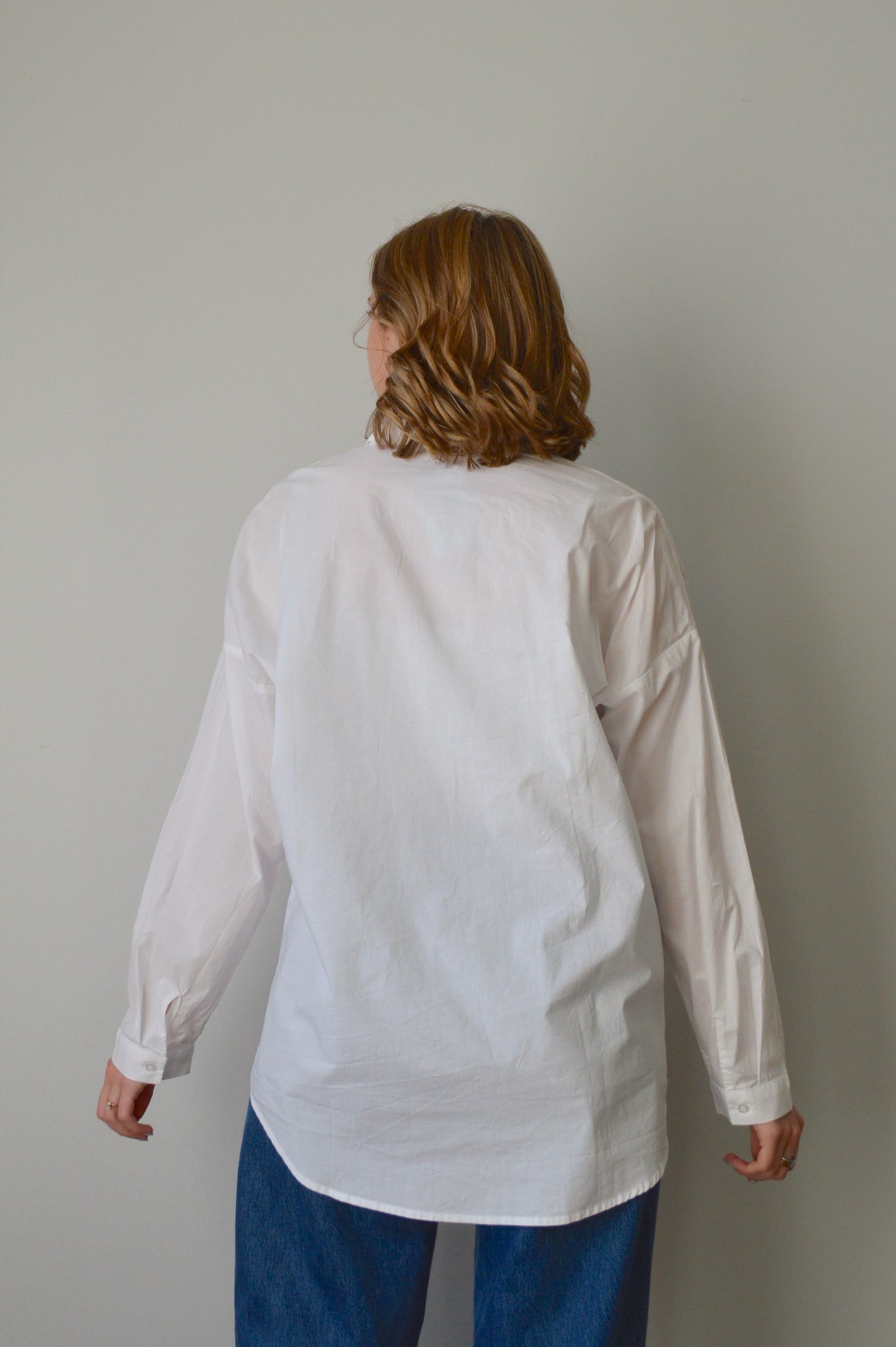 Person wearing a white button down shirt and blue jeans on a plain background