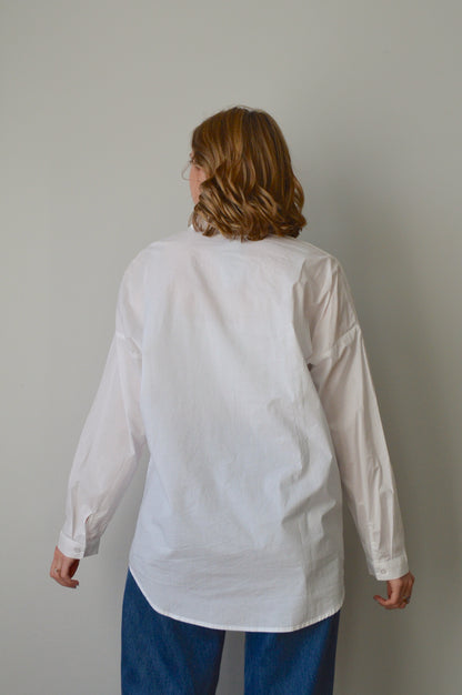 Person wearing a white button down shirt and blue jeans on a plain background