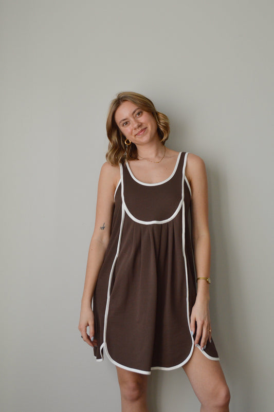 Woman wearing a brown dress with white trim against a plain background