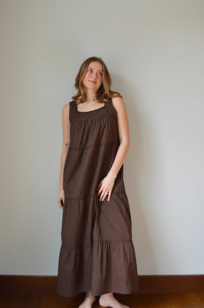 Woman wearing a brown dress standing against a plain wall.