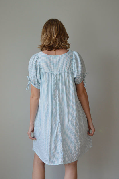 Woman wearing a light striped blue dress against a plain background