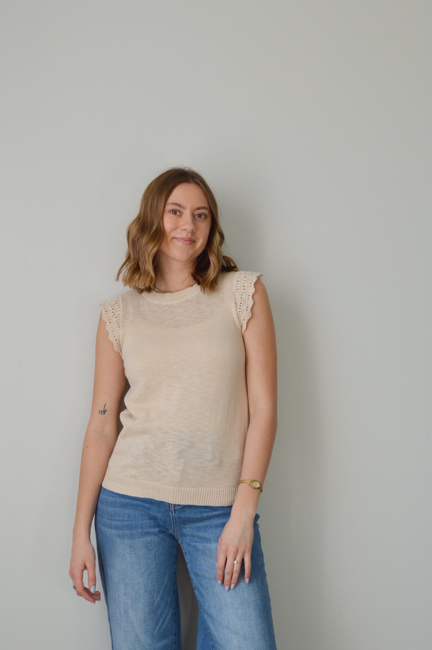 Woman wearing a beige top and blue jeans against a plain background