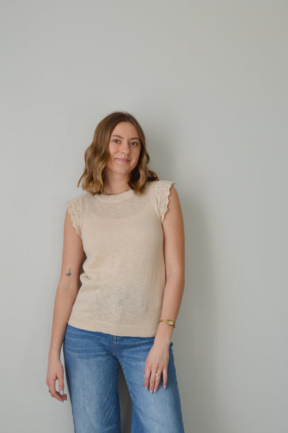 Woman wearing a beige top and blue jeans against a plain background