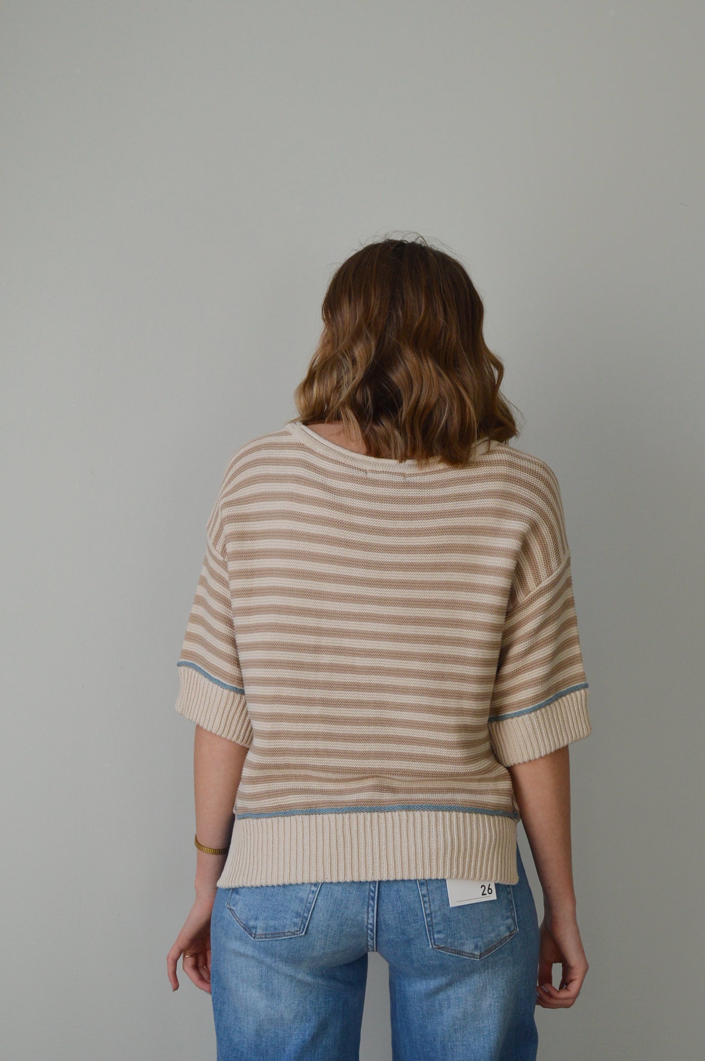 Woman wearing a tan striped sweater and blue jeans against a plain background