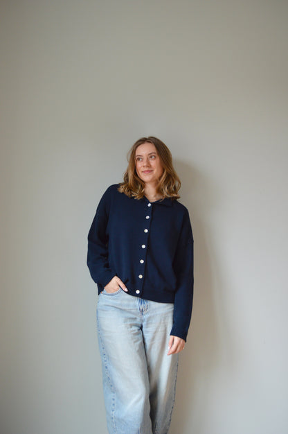 Person wearing a navy cardigan with pearl buttons on a plain background