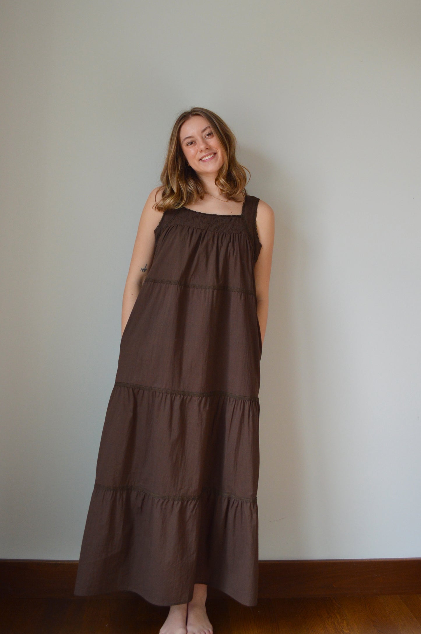 Woman wearing a brown dress standing against a plain wall.
