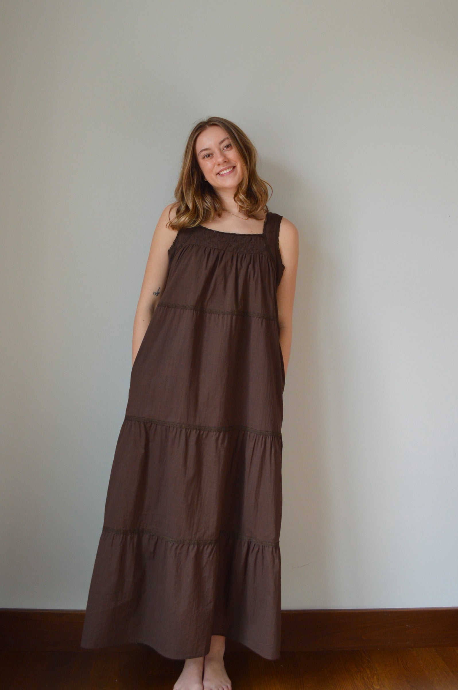 Woman wearing a brown dress standing against a plain wall.