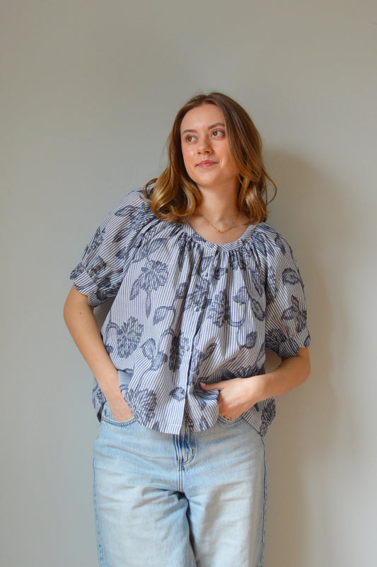 Woman wearing a blue striped blouse with navy floral design and jeans against a plain background