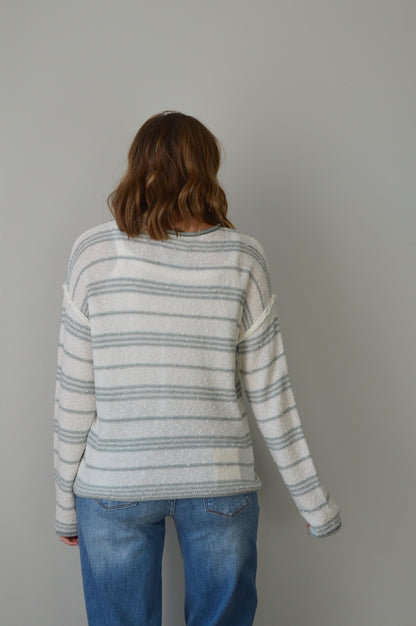 Person wearing a blue striped sweater and jeans on a plain background