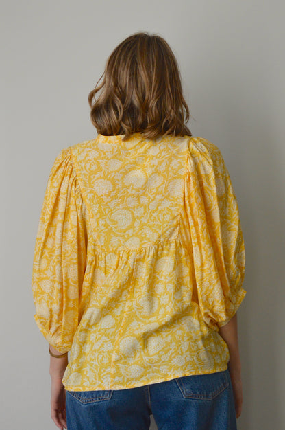Person wearing a yellow patterned top with blue jeans on a plain background