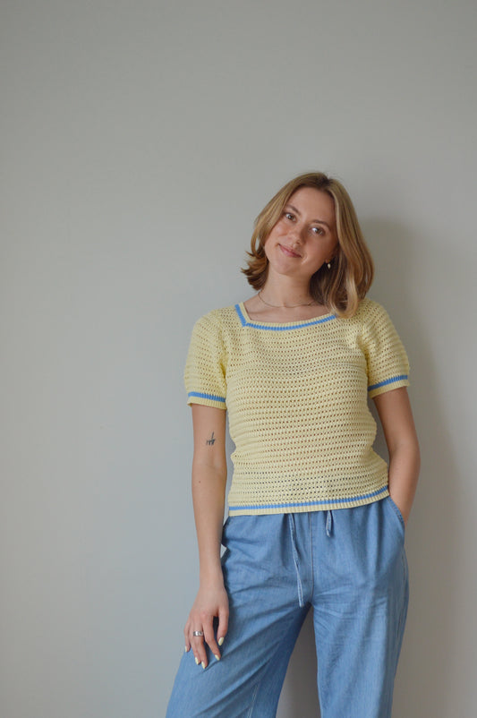 Woman wearing a yellow top and blue pants against a plain background
