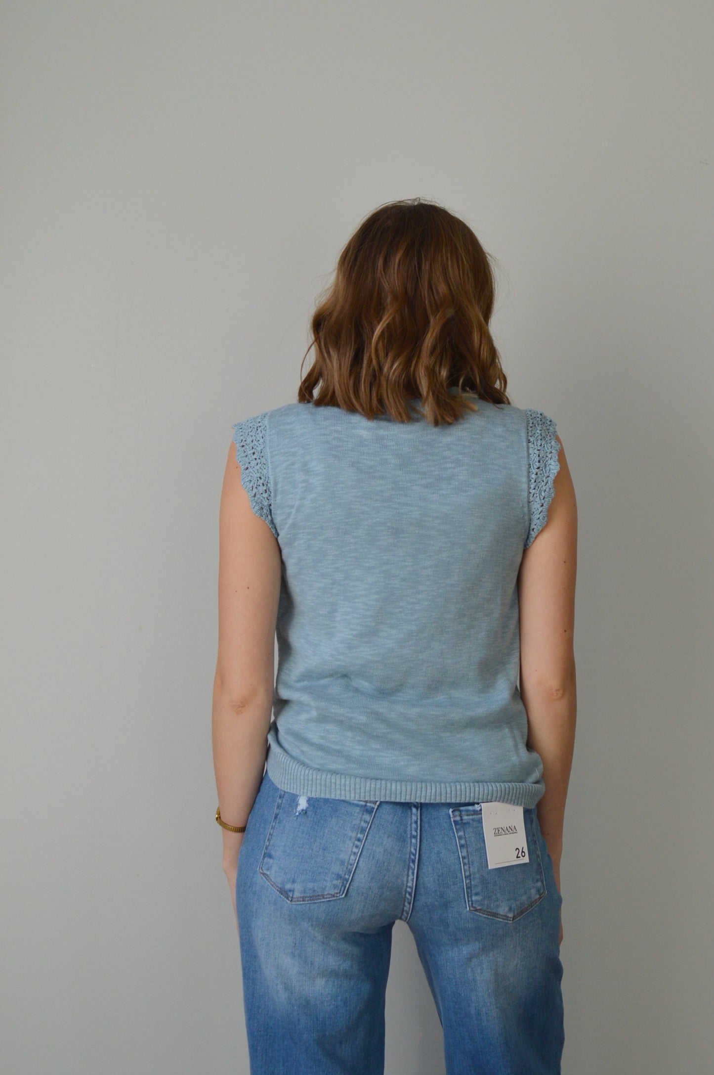 Woman wearing a light blue top and jeans on a plain background