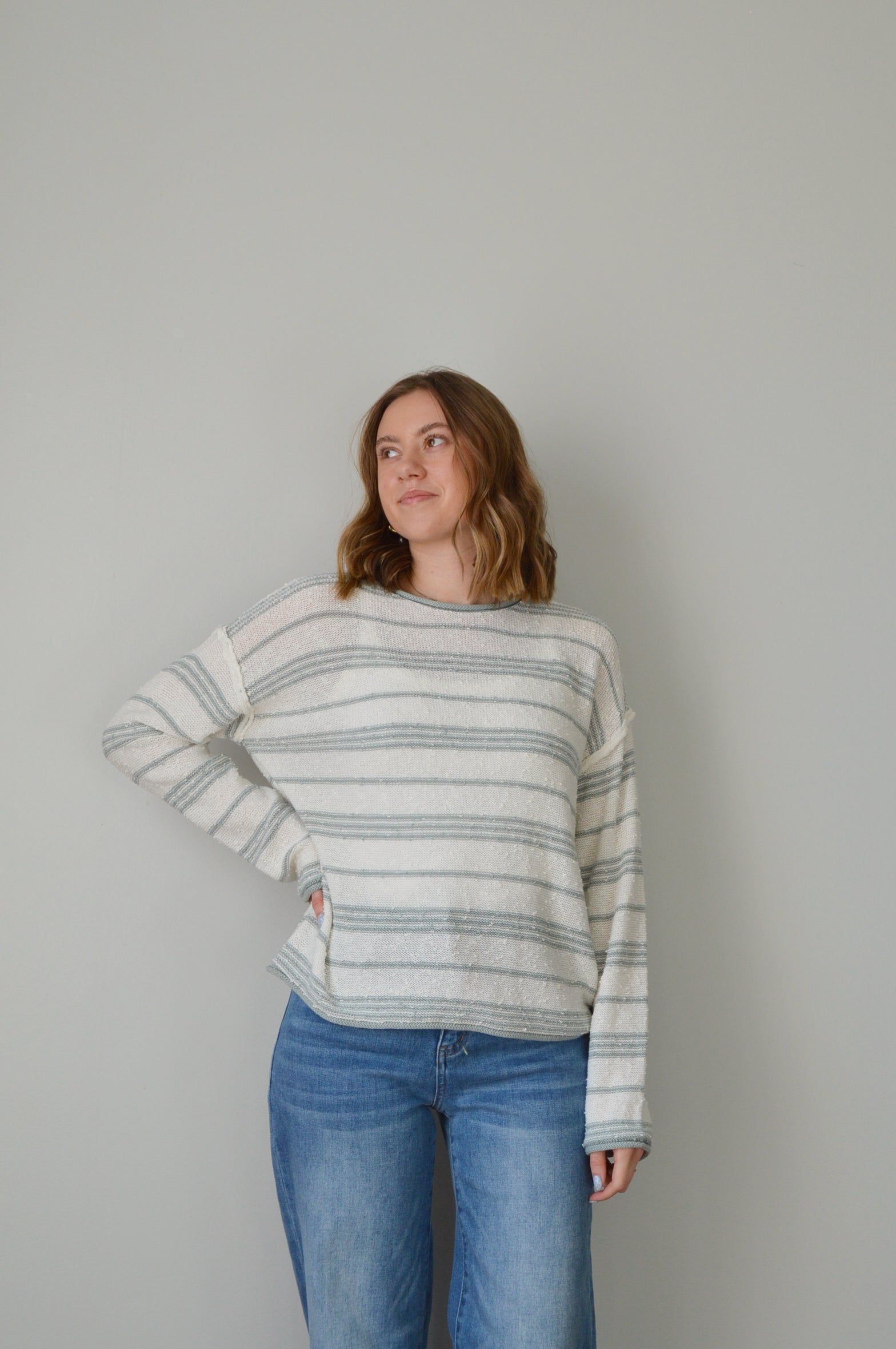 Person wearing a blue striped sweater and jeans on a plain background