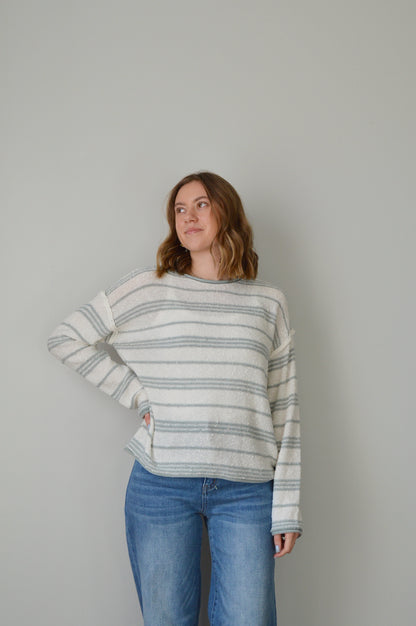 Person wearing a blue striped sweater and jeans on a plain background