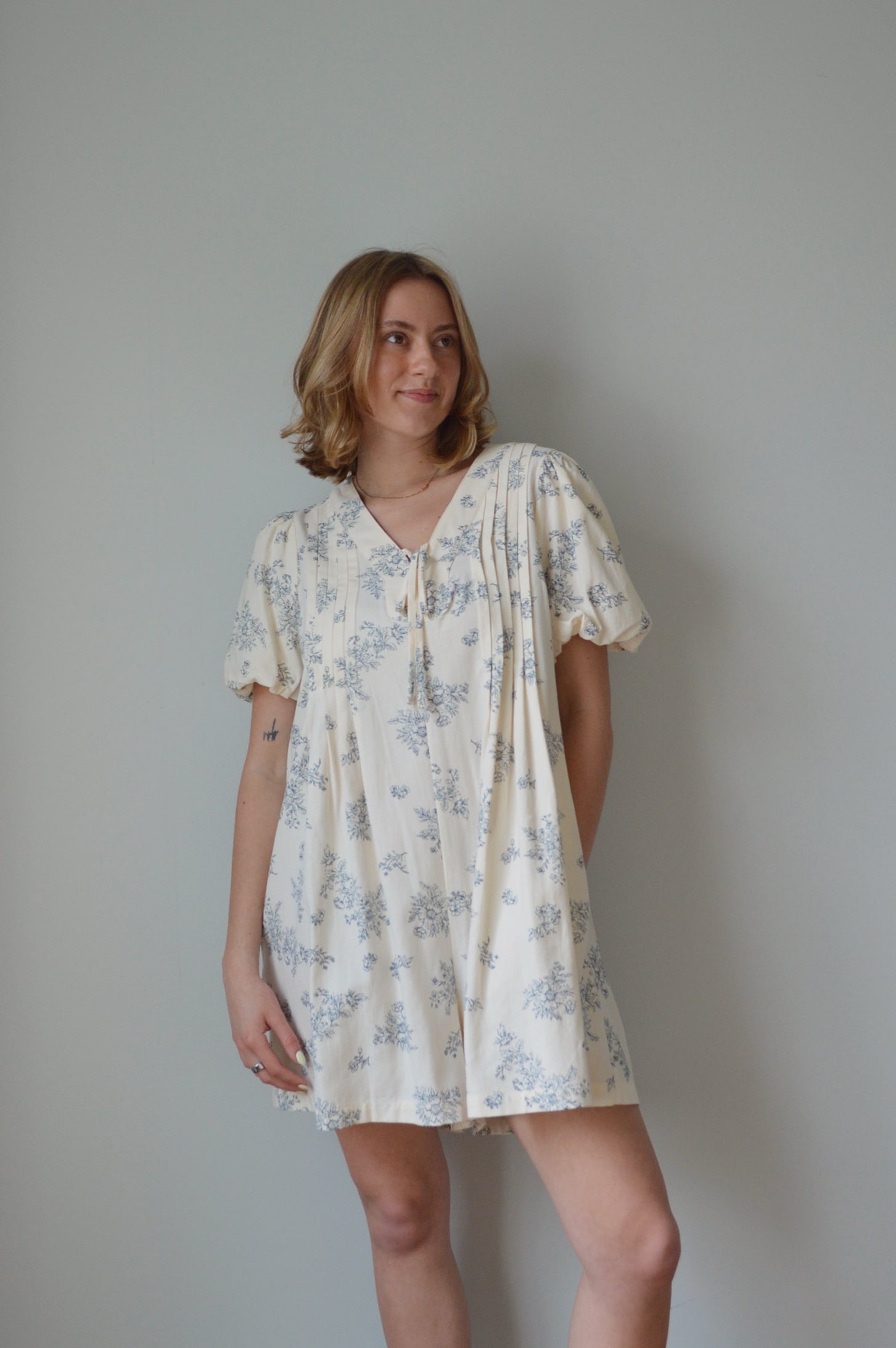 Woman wearing a cream romper with a blue floral pattern against a plain background 