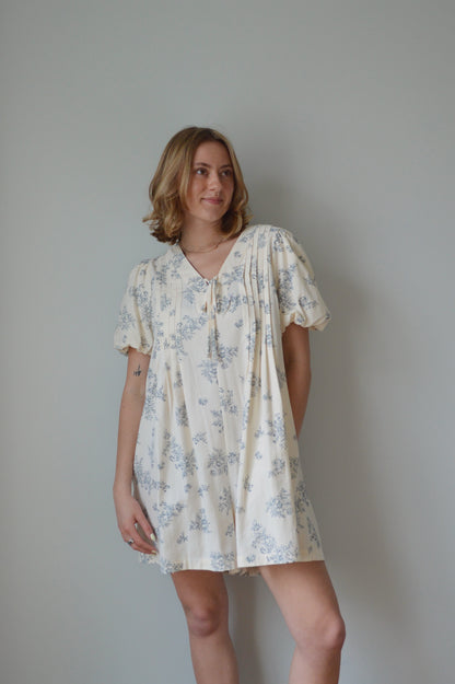Woman wearing a cream romper with a blue floral pattern against a plain background 
