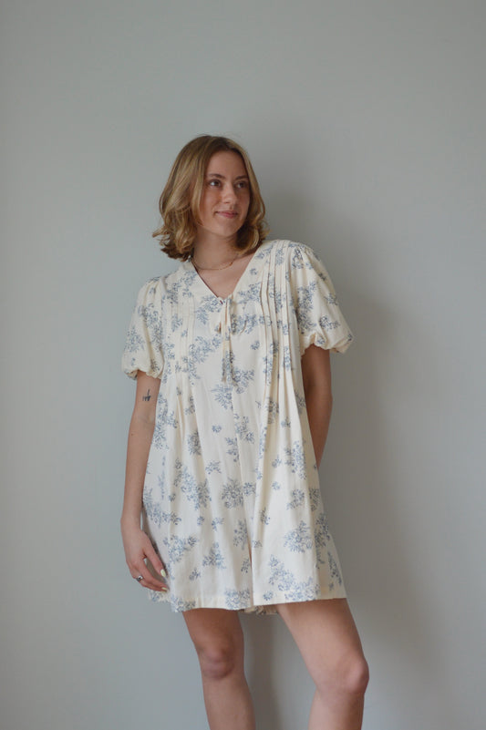 Woman wearing a cream romper with a blue floral pattern against a plain background 