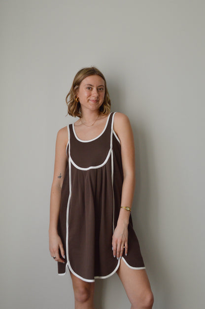 Woman wearing a brown dress with white trim on a plain background