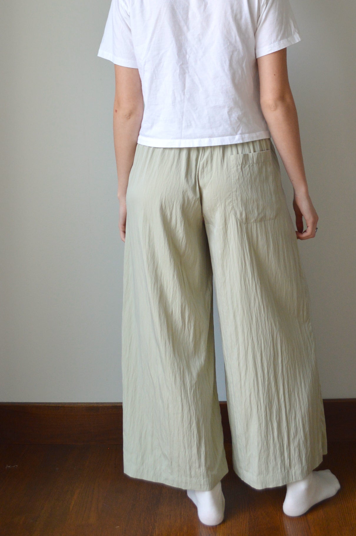 Person wearing a white top and light green pants on a plain background
