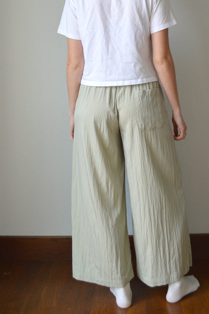 Person wearing a white top and light green pants on a plain background