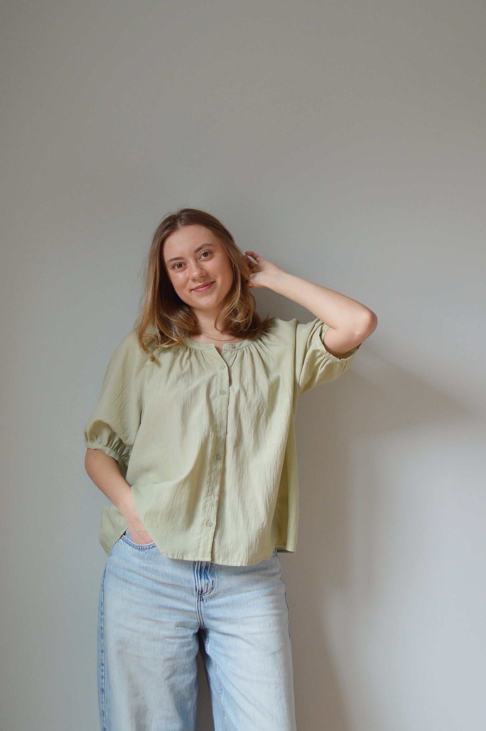 Woman wearing a light green blouse and blue jeans against a plain background