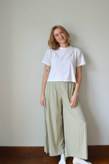 Person wearing a white top and light green pants on a plain background