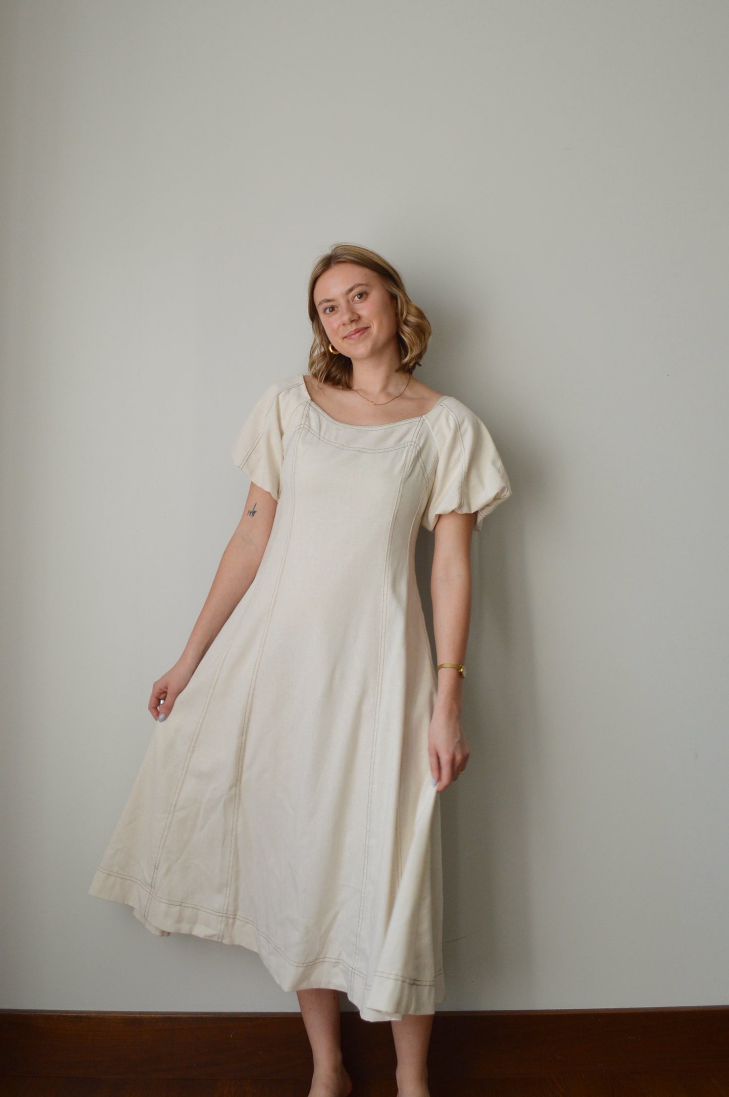Woman wearing a cream dress standing against a plain background
