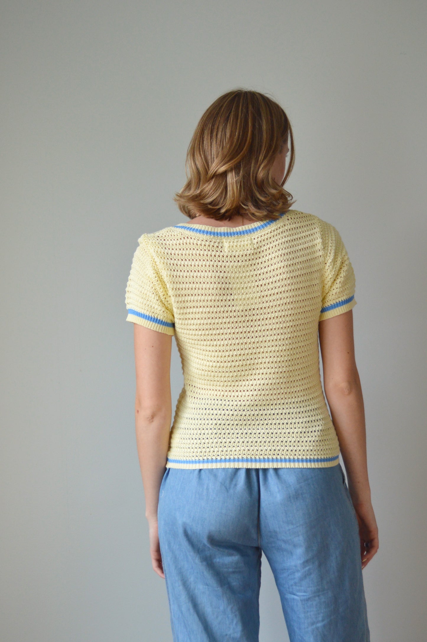 Woman wearing a yellow top and blue pants against a plain background
