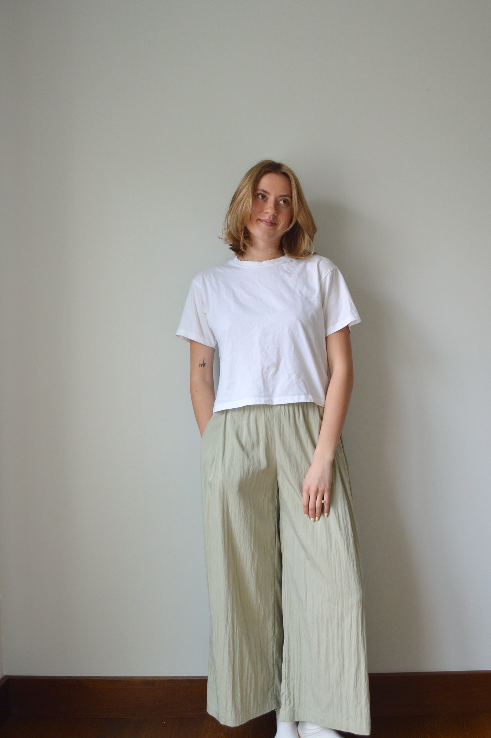 Person wearing a white top and light green pants on a plain background