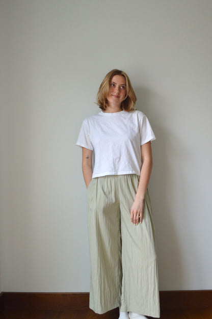Person wearing a white top and light green pants on a plain background
