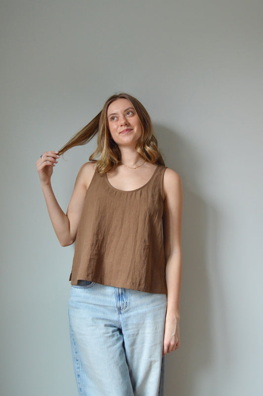 Woman in a brown tank top and blue jeans standing against a plain background