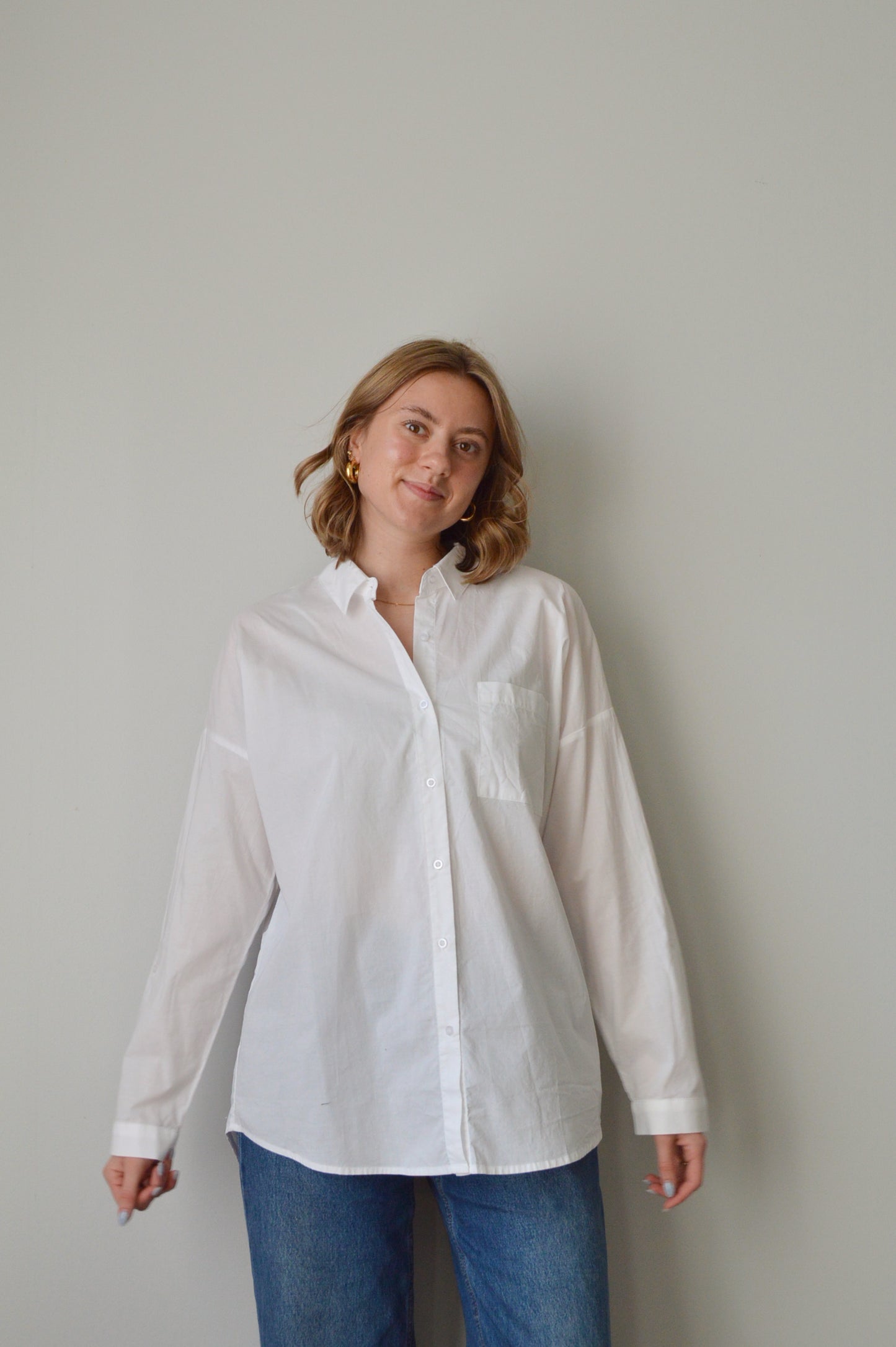 Person wearing a white button down shirt and blue jeans on a plain background