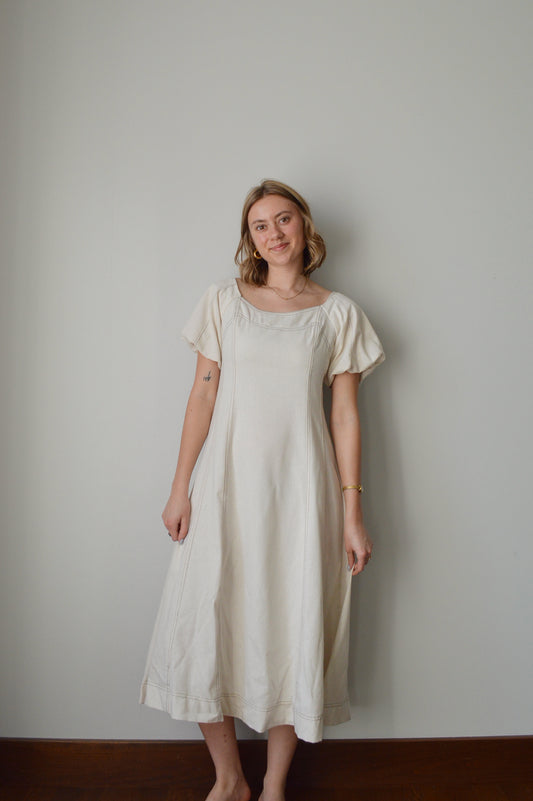 Woman wearing a cream dress standing against a plain background