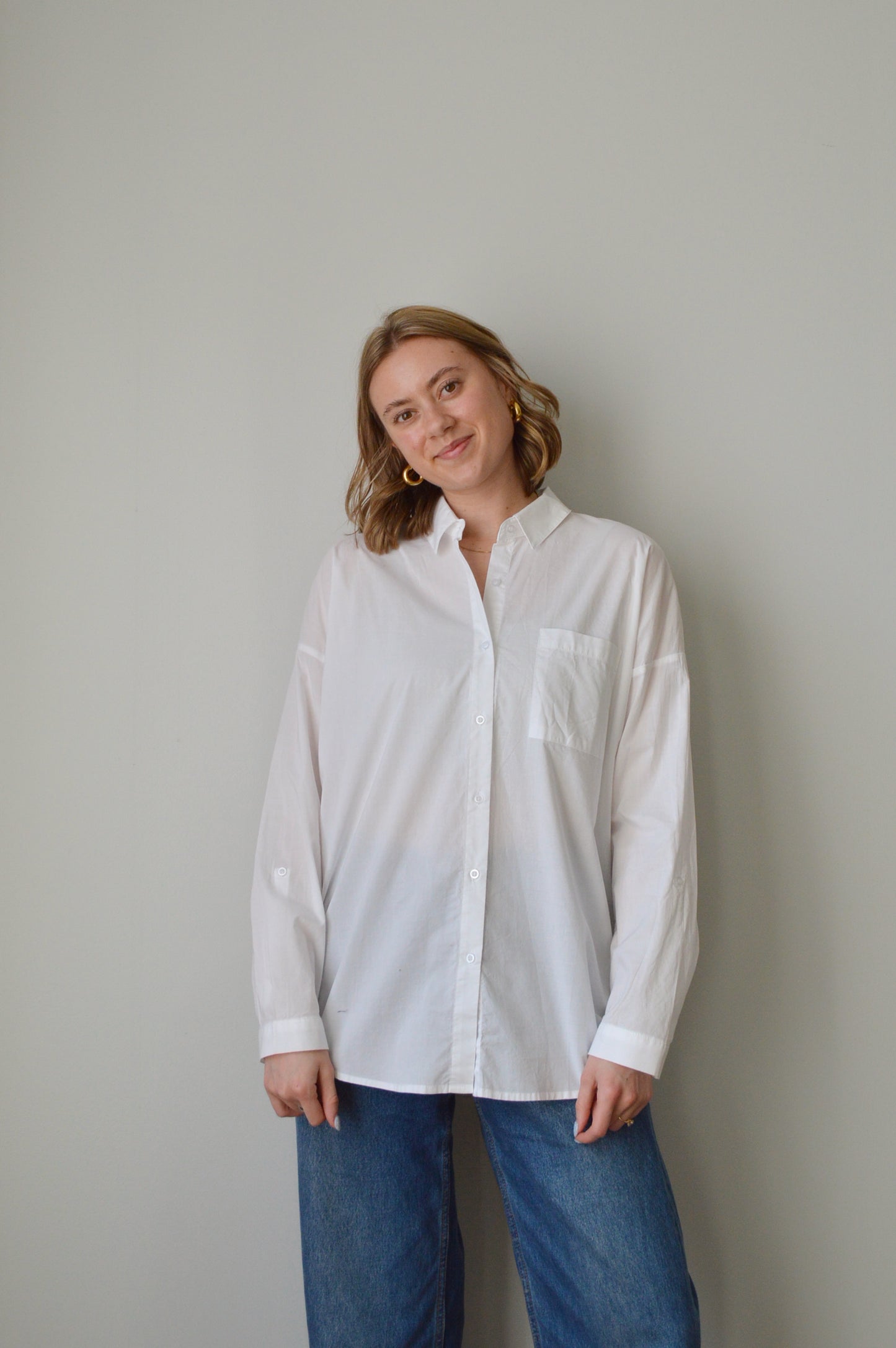 Person wearing a white button down shirt and blue jeans on a plain background