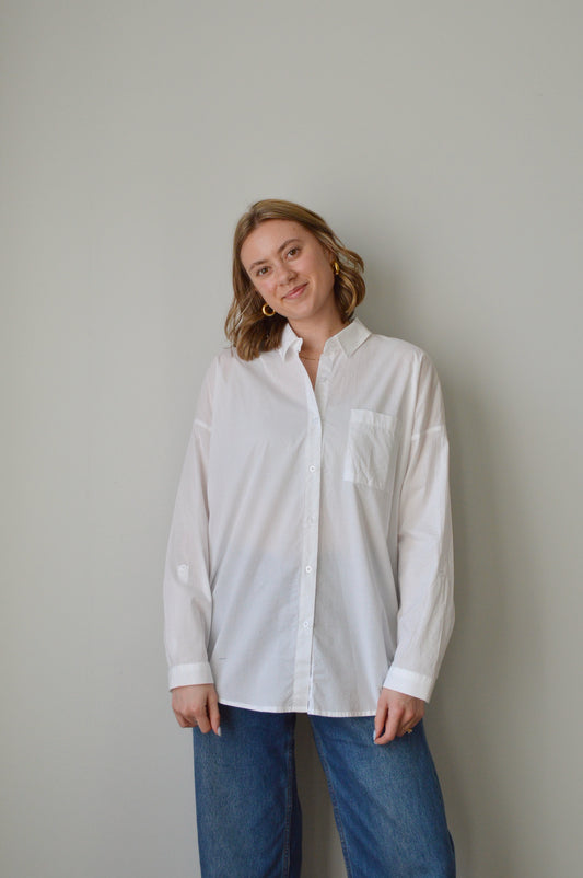 Person wearing a white button down shirt and blue jeans on a plain background