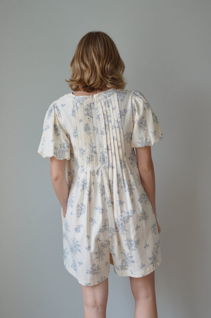 Woman wearing a cream romper with a blue floral pattern against a plain background 